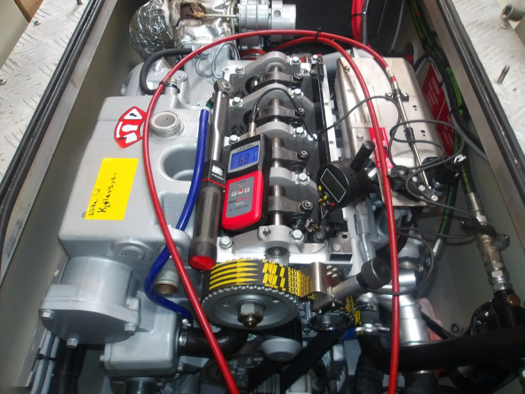 Et nærbilde av en motor med synlige komponenter, ulike kabler og en digital måler som viser en avlesning på 6.84 plassert på toppen.