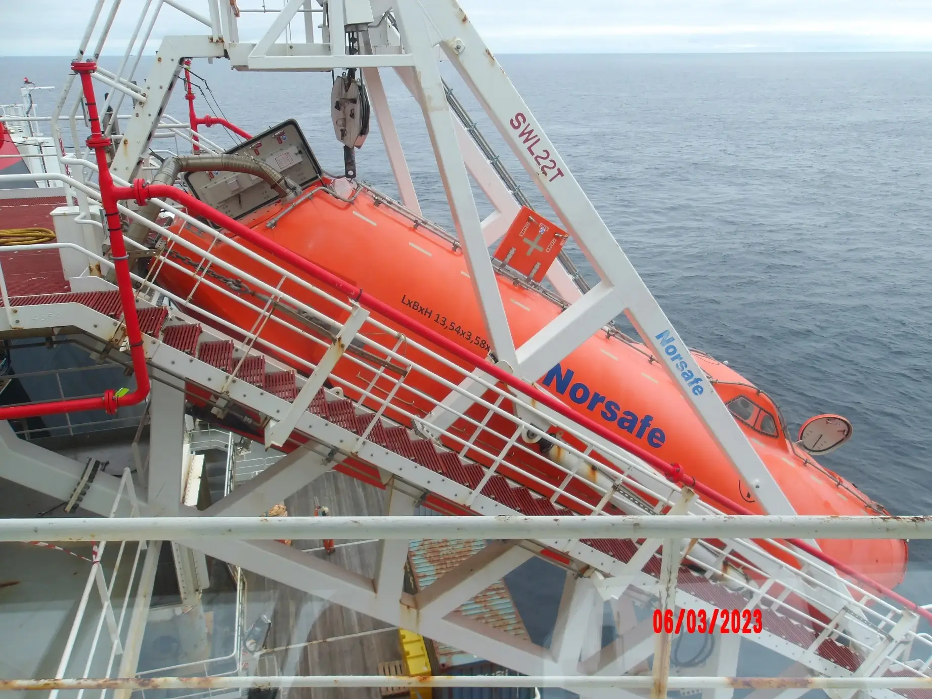 En oransje livbåt firenes ned fra dekket og ned i sjøen, mens sikkerhetsutstyr og metallstrukturer omgir den.