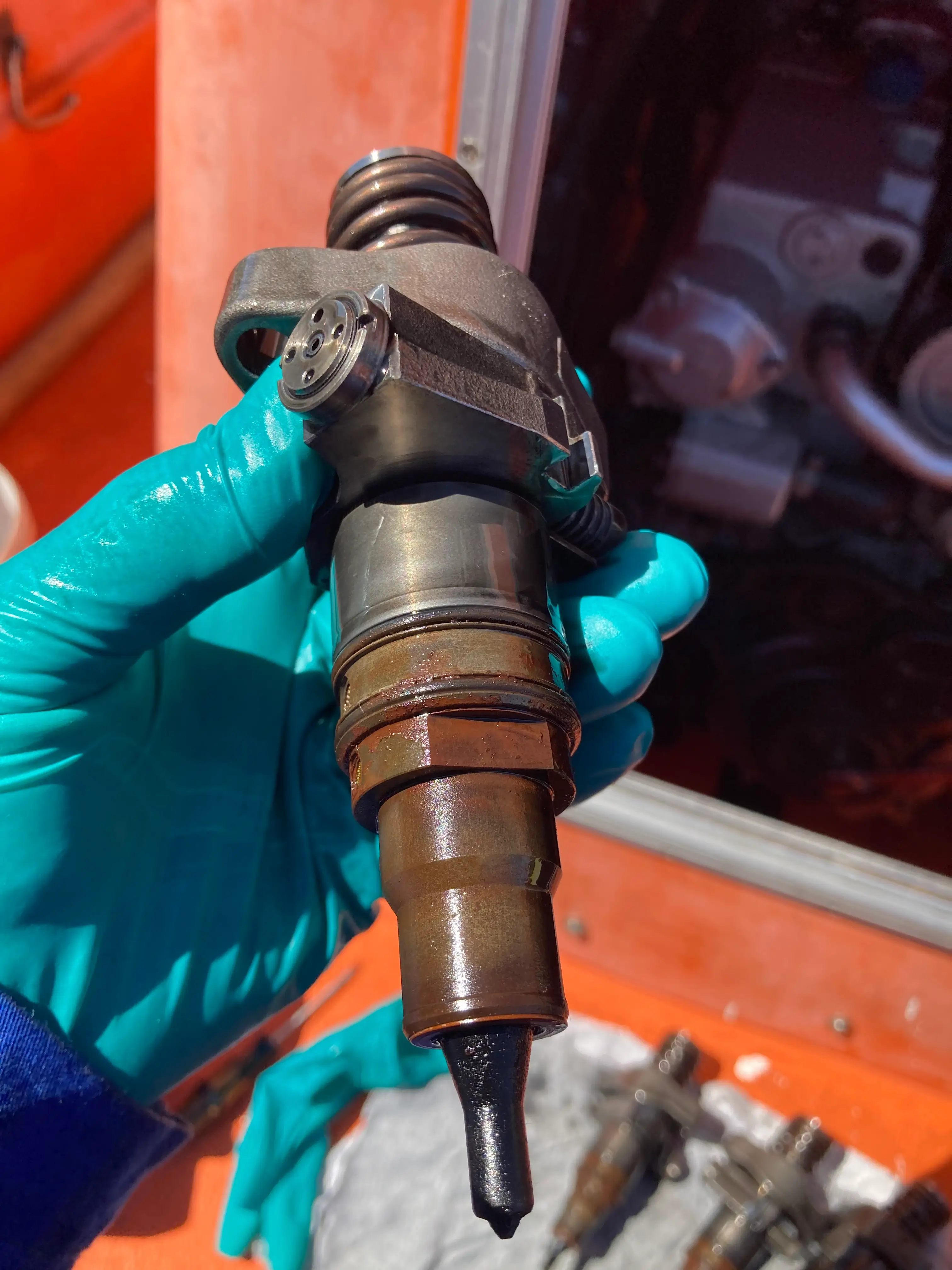 En person med blå hansker holder en drivstoffinjektor, viser tippen og tilkoblingene..